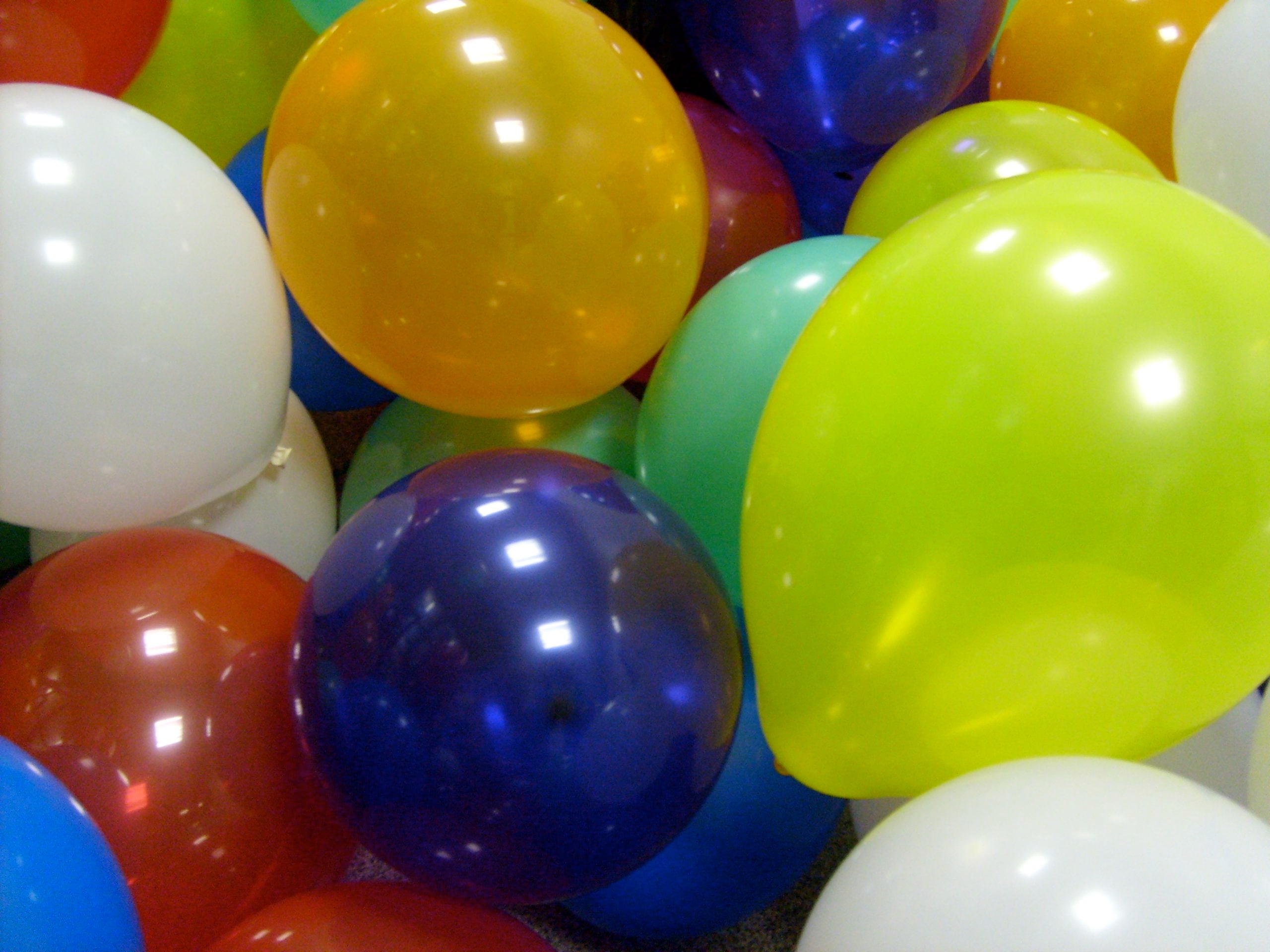 A pile of colorful balloons, including yellow, blue, orange, white, red, and green, clustered closely together, filling the frame.