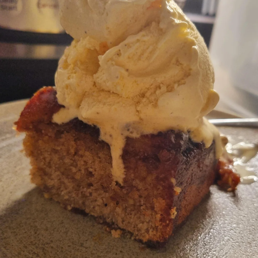 A slice of moist banana bread topped with a scoop of vanilla ice cream, slightly melting, served on a plate.