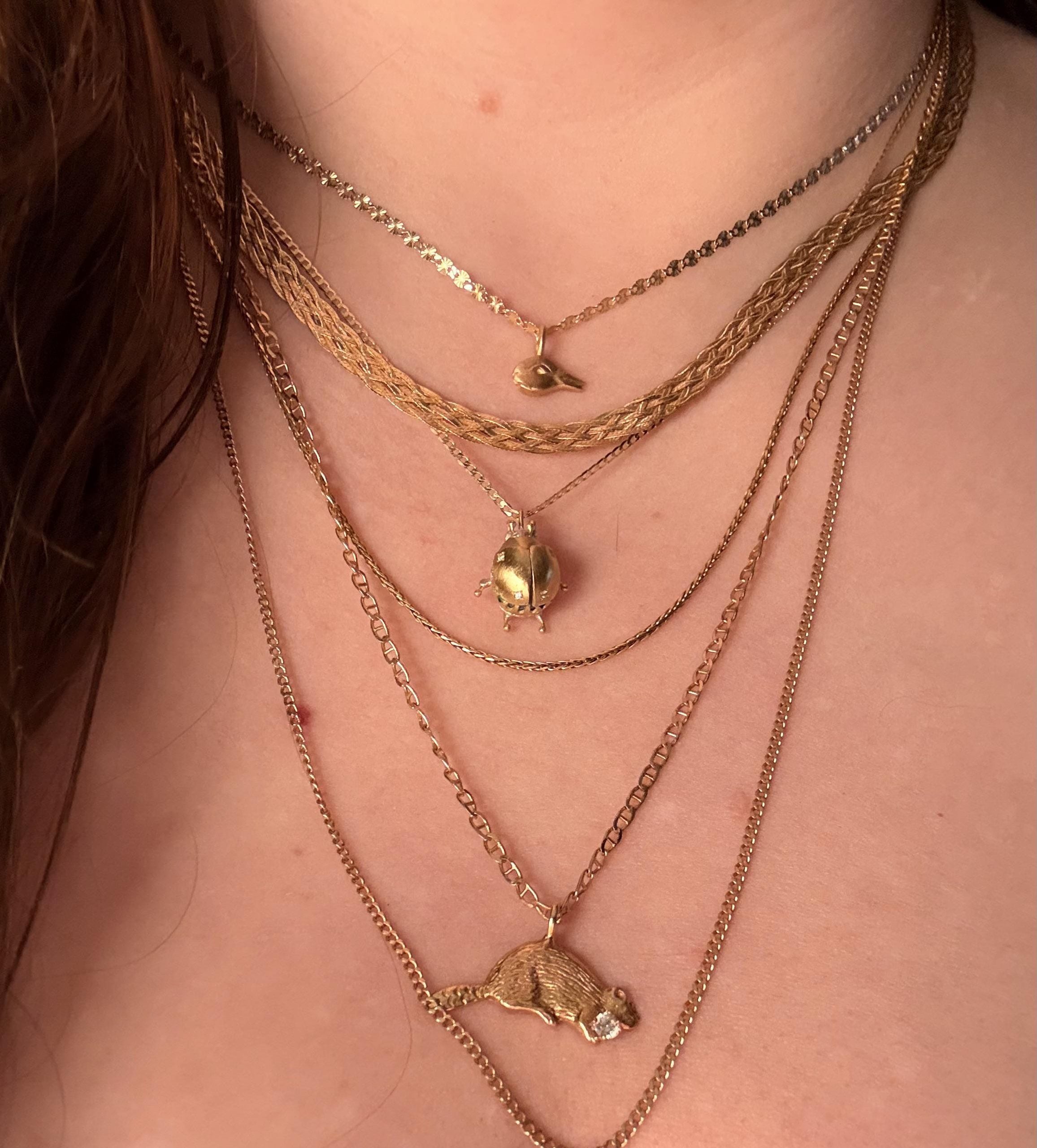 A close-up of a person’s neck wearing five layered gold necklaces, each with a unique pendant: a whale tail, a leaf, and a beaver, with different chain styles and lengths.