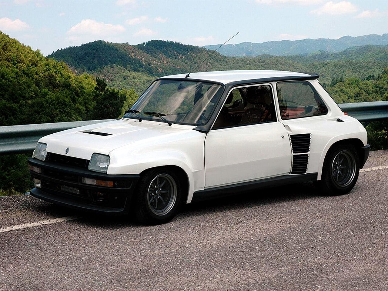 A white classic hatchback car with black accents is parked on a road with a metal guardrail, surrounded by green hills under a blue sky.