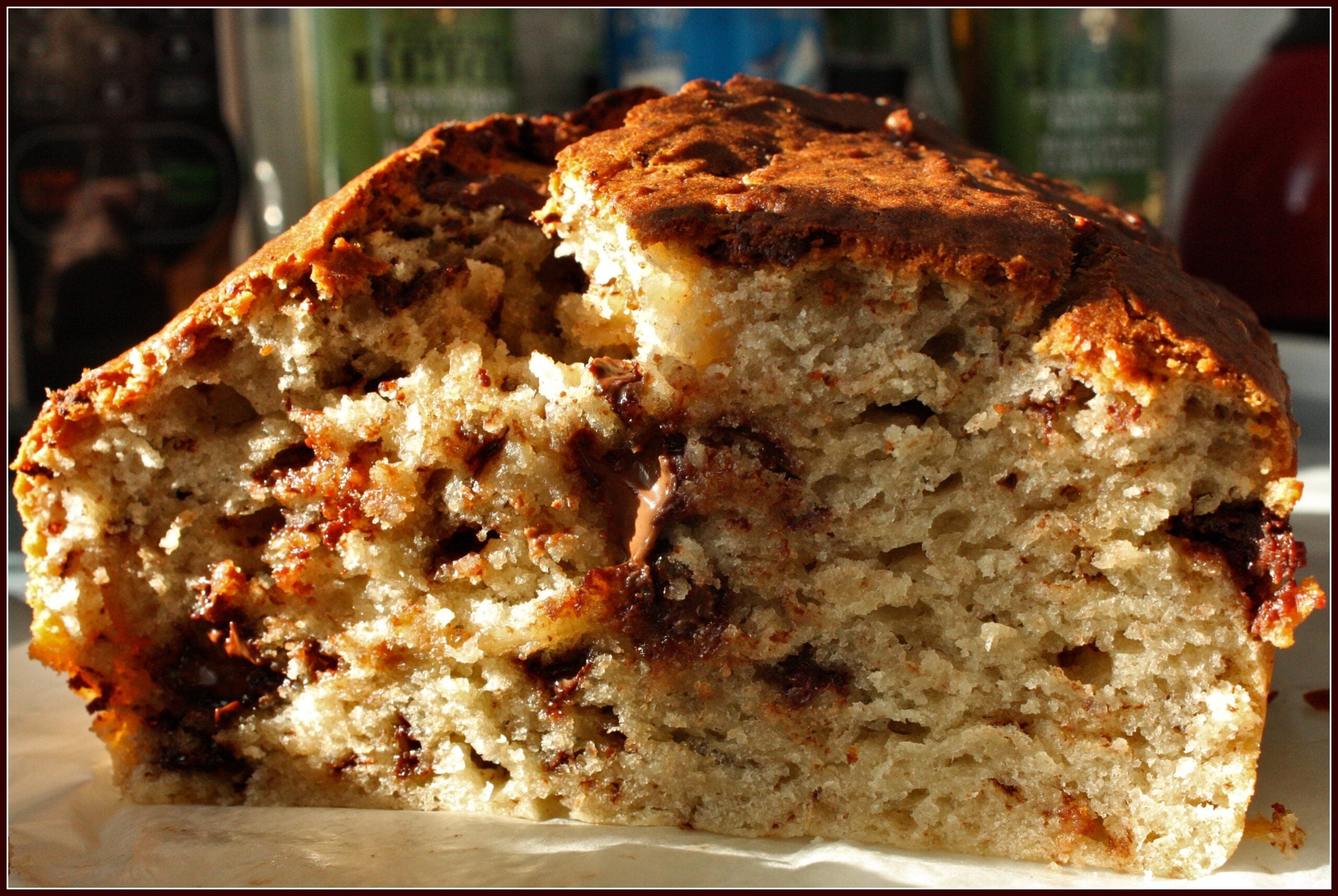 A close-up of a thick slice of banana bread with chocolate chips, showing a moist and dense interior and a golden-brown crust.