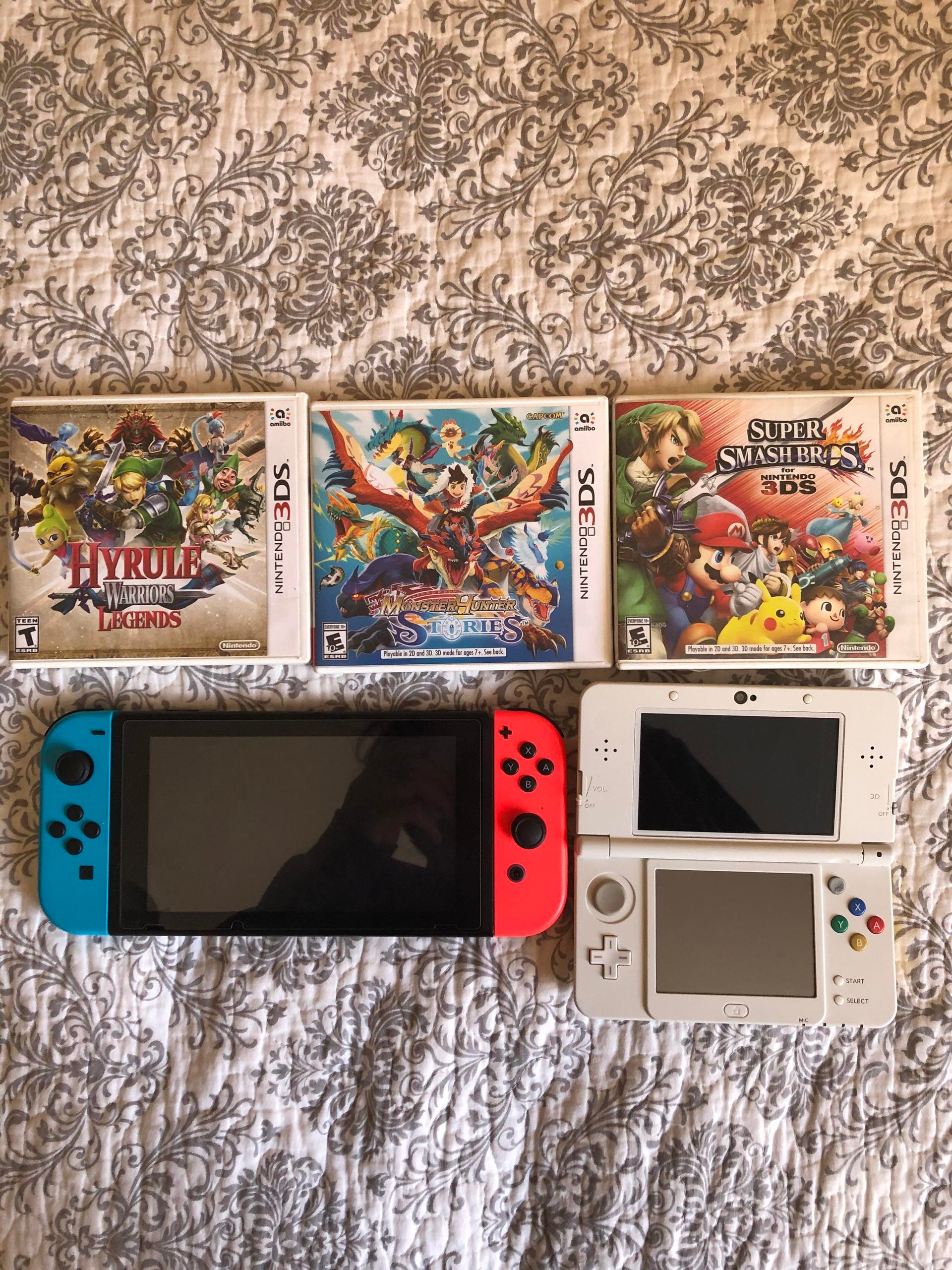 Three Nintendo 3DS game cases and cartridges are above a Nintendo Switch and a white Nintendo 3DS XL, all on a beige patterned bedspread.