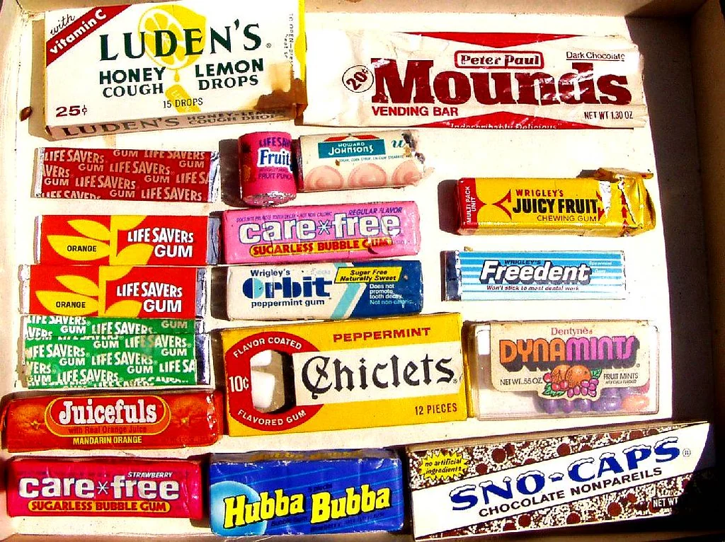 A box filled with various vintage candy and gum packages, including Luden’s, Mounds, Carefree, Life Savers, Chiclets, Hubba Bubba, Sno-Caps, Juicefuls, and others, arranged in rows.