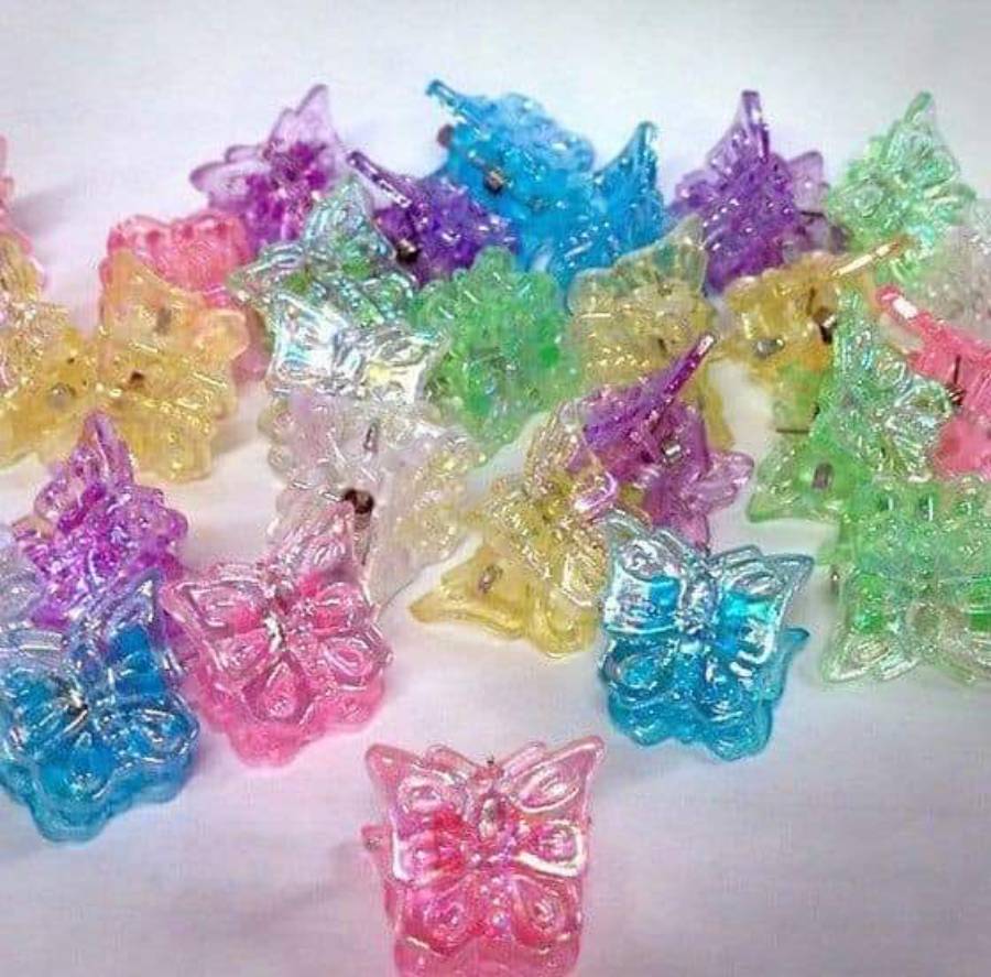 A collection of small, translucent butterfly-shaped hair clips in various pastel colors, including pink, purple, yellow, green, and blue, spread out on a white surface.