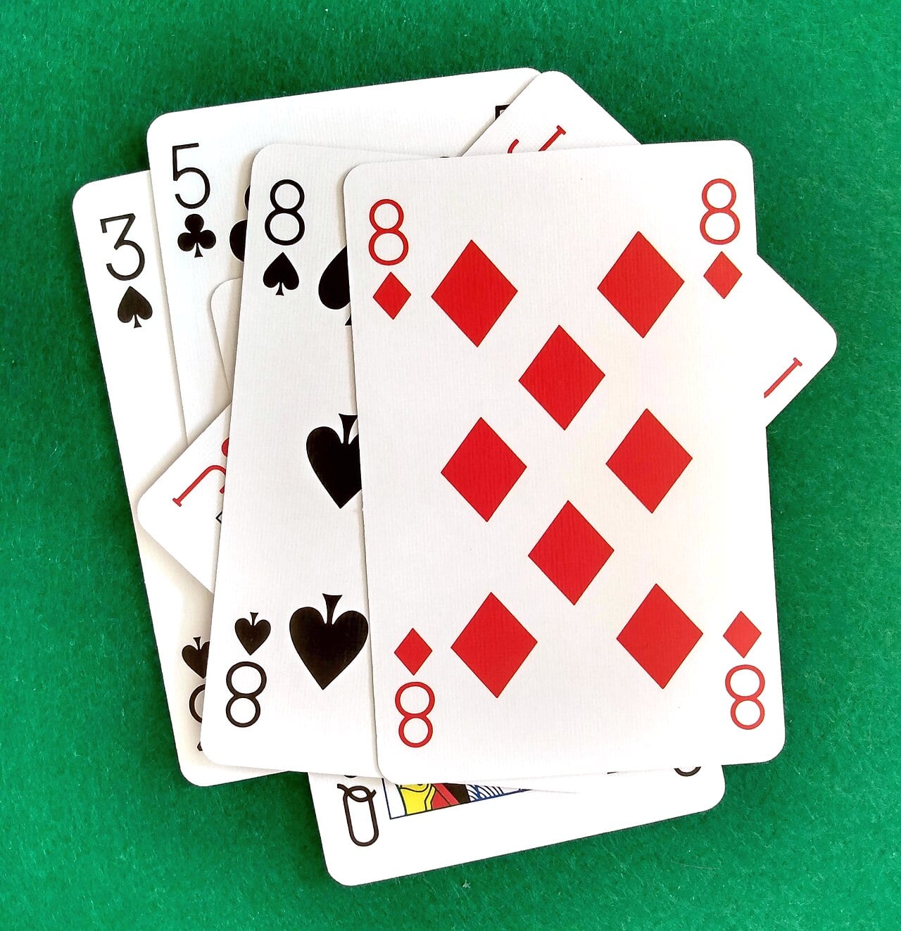 Five playing cards—the 8 of diamonds, 8 of spades, 8 of clubs, 3 of clubs, and the queen of spades—are fanned out on a green felt surface.