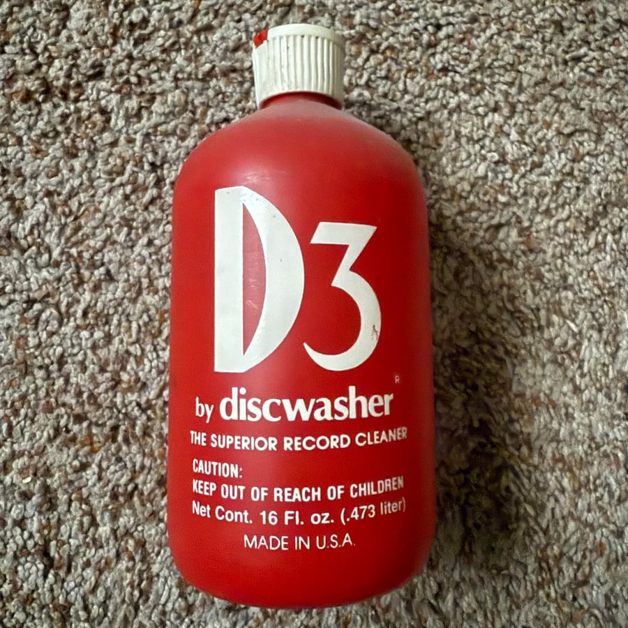 A red bottle labeled “D3 by discwasher, The Superior Record Cleaner,” lying on carpet. The bottle holds 16 fl. oz. and cautions to keep out of reach of children. Made in the USA.