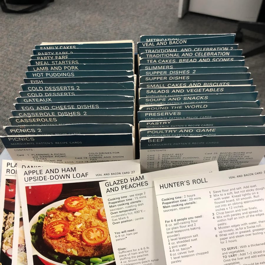 A recipe card index is shown, with labeled dividers for categories like cakes, puddings, eggs, beef, and more. Two open recipe cards display instructions for “Apple and Ham Upside-Down Cake” and “Hunter’s Roll.”