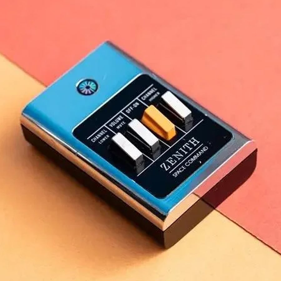 A vintage Zenith Space Command remote control with three silver and one yellow button sits on a diagonal background split between orange and peach colors.