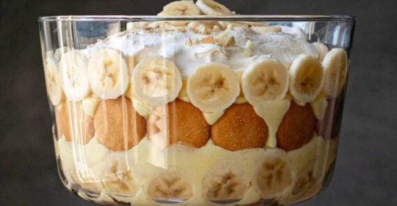 A glass trifle dish filled with layers of banana slices, vanilla wafers, creamy pudding, and whipped topping, garnished with banana slices on top.