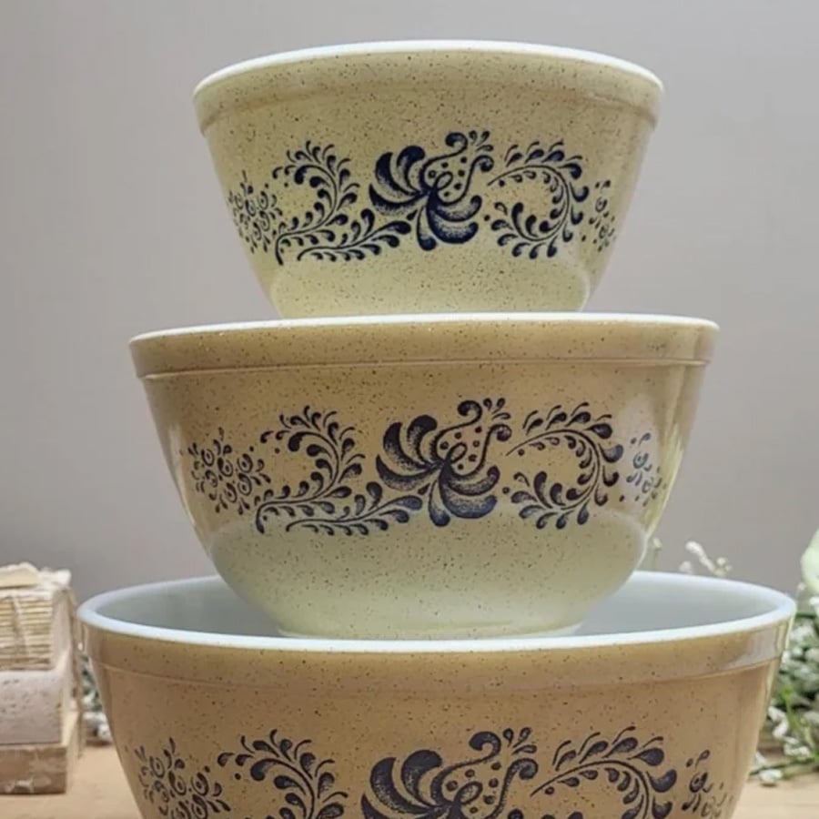 Three vintage mixing bowls with a blue floral design are stacked on top of each other against a neutral background.