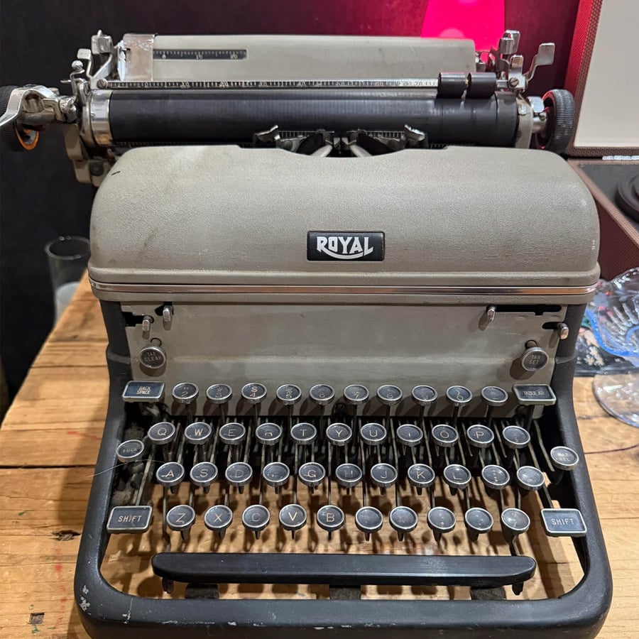 A vintage Royal typewriter sits on a wooden table. The keys and levers are visible, and the surface shows signs of age and use.