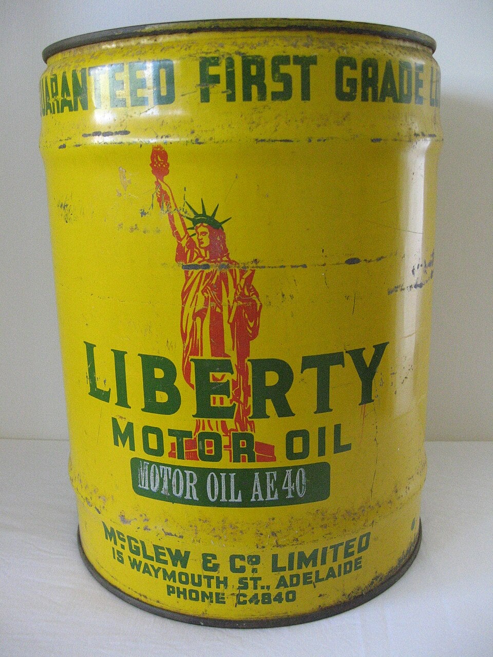 A yellow vintage Liberty Motor Oil can with a green Statue of Liberty graphic and green text, showing signs of age and wear. Manufacturer details are printed on the lower part of the can.