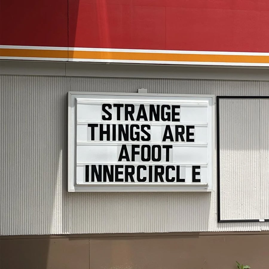 A marquee sign on a wall reads, “STRANGE THINGS ARE AFOOT INNERCIRCLE.” The sign has black letters on a white background.