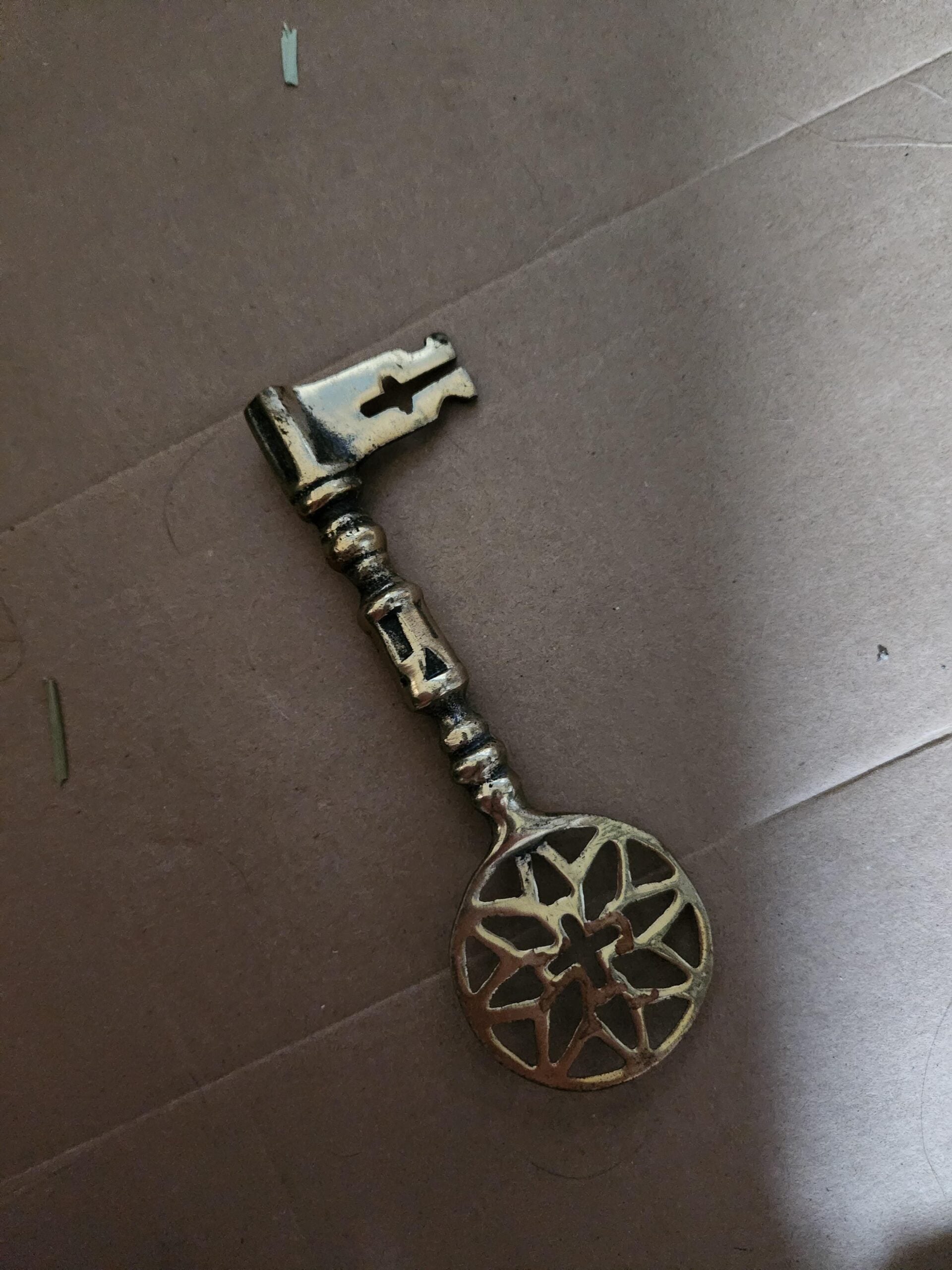 A vintage-style brass key with a decorative, star-shaped design on the bow lies on a brown cardboard surface.