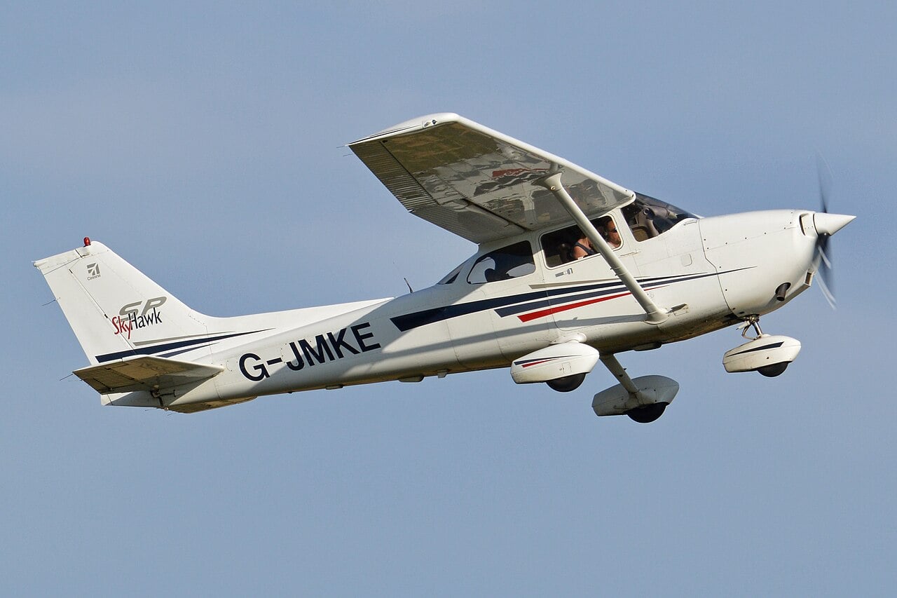 A white single-engine propeller airplane with registration G-JNKE is flying in a clear blue sky.