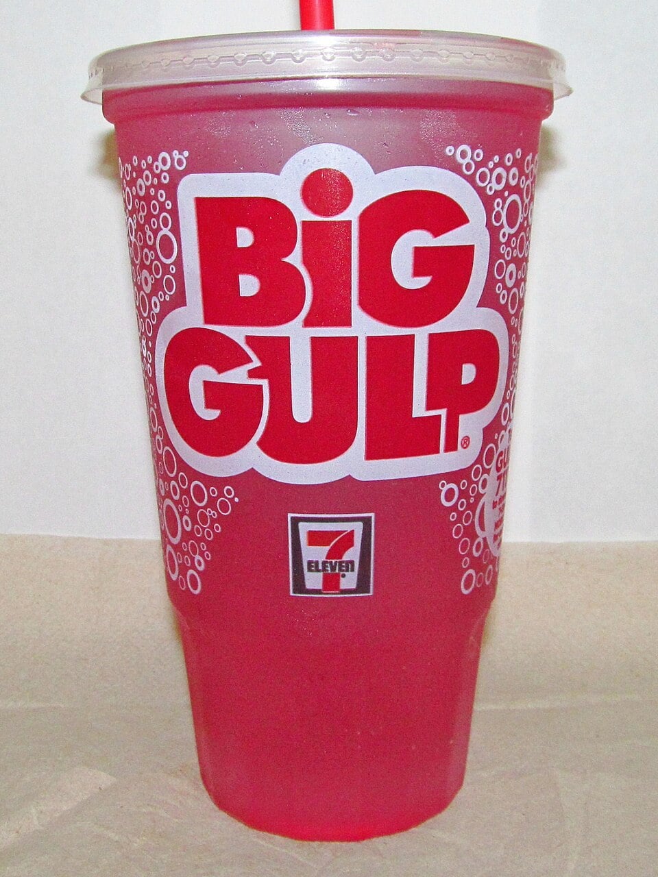A large plastic cup with the words “BIG GULP” in bold white and red letters, filled with a red beverage and a red straw, featuring the 7-Eleven logo on the front.