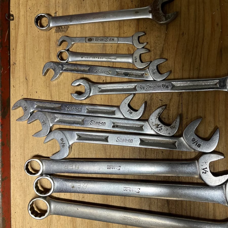 A set of metal Snap-on wrenches of various sizes are arranged on a wooden surface, with both open-end and box-end visible.