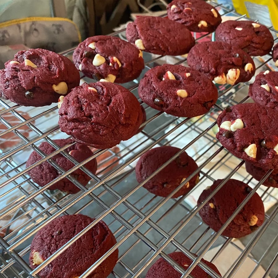 Red velvet cookies with white chocolate chips cooling on metal racks in a kitchen setting.