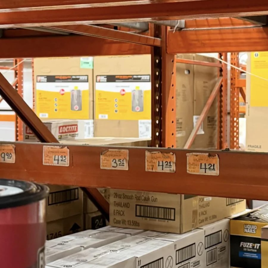 Shelves in a hardware store are stocked with boxes labeled “Loctite” and various price tags, including $3.21, $4.21, and $9.99, are visible on the orange shelf edge.