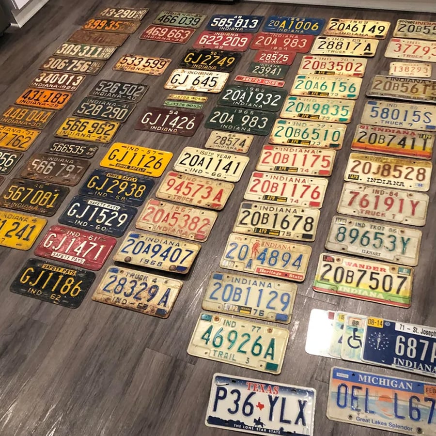 A collection of vintage license plates from various states, arranged neatly on a wooden floor in rows and columns, displaying different colors, fonts, and years.
