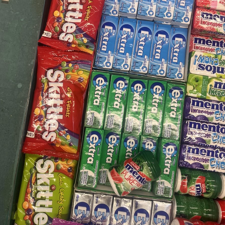 A store shelf displays Skittles bags, Extra gum packs, and Mentos containers in colorful packaging, neatly arranged in rows.