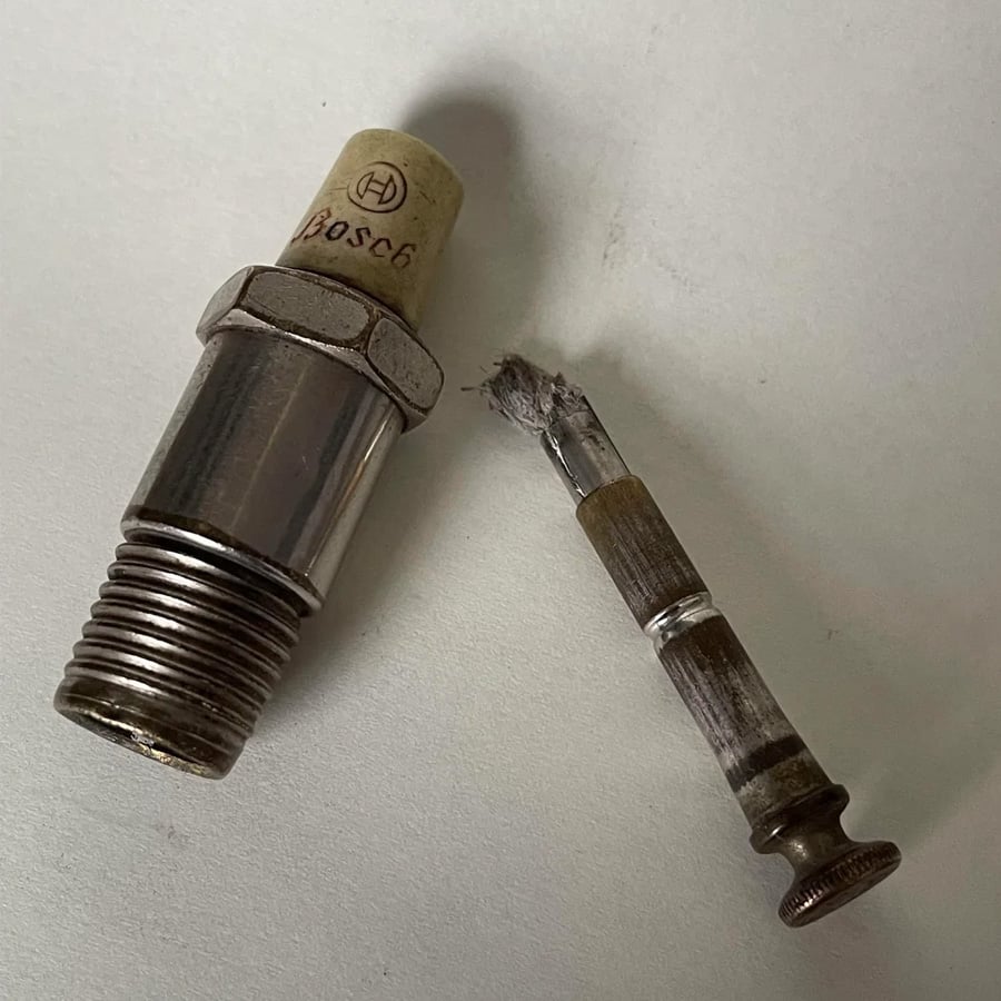 A broken spark plug with the threaded metal shell on the left and the separated central electrode and insulator on the right, both resting on a white surface.