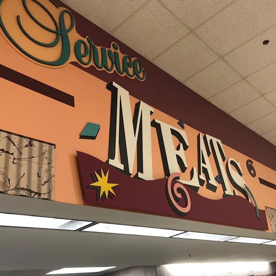 A colorful sign inside a store reads “Service Meats” in large, stylized letters against a peach and maroon background with decorative geometric shapes.