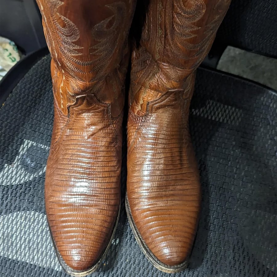 A pair of brown leather cowboy boots with a textured, reptile-like pattern, resting on a black mesh chair.