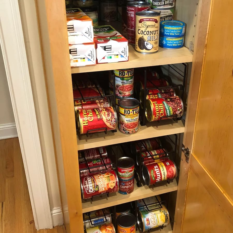 A pantry cabinet with shelves stocked with canned foods like Ro-Tel, coconut milk, chili, and chipotle peppers, plus boxed items and canned chicken breast on the top shelf.