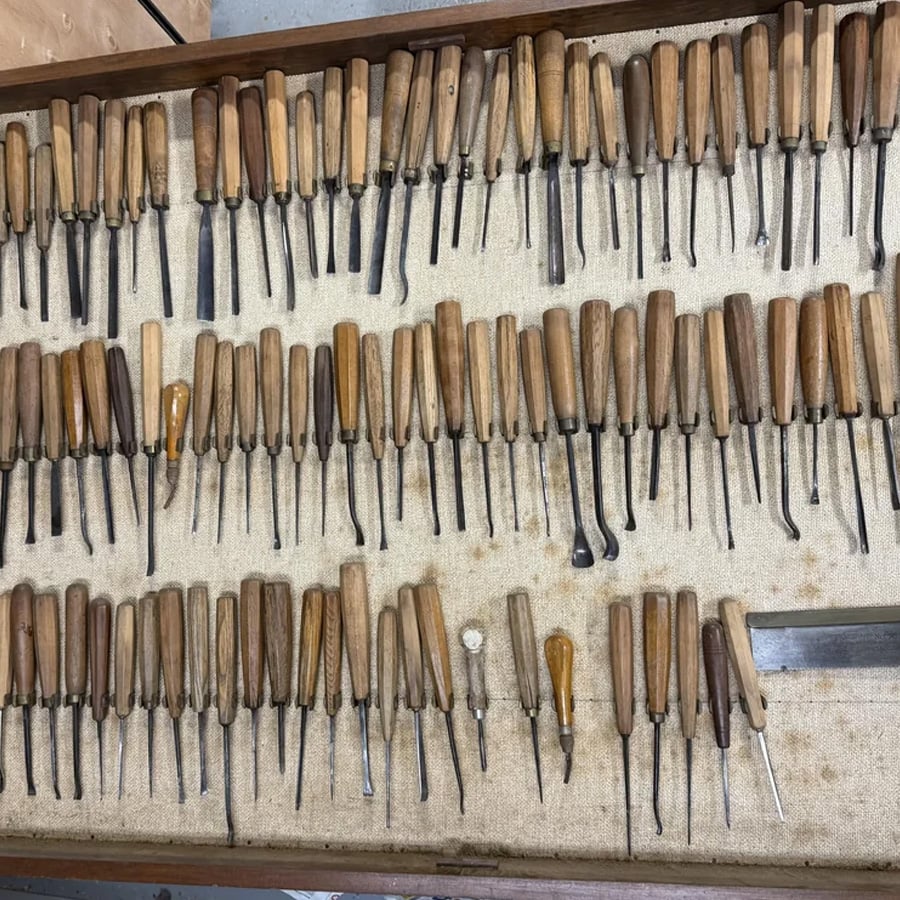 A collection of various wood carving tools with wooden handles neatly arranged in rows on a fabric-lined tray.