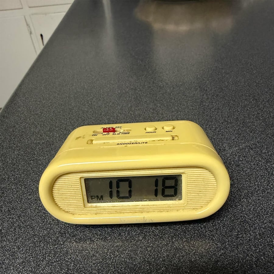 A yellow digital alarm clock shows the time as 10:18 PM while sitting on a gray speckled countertop.