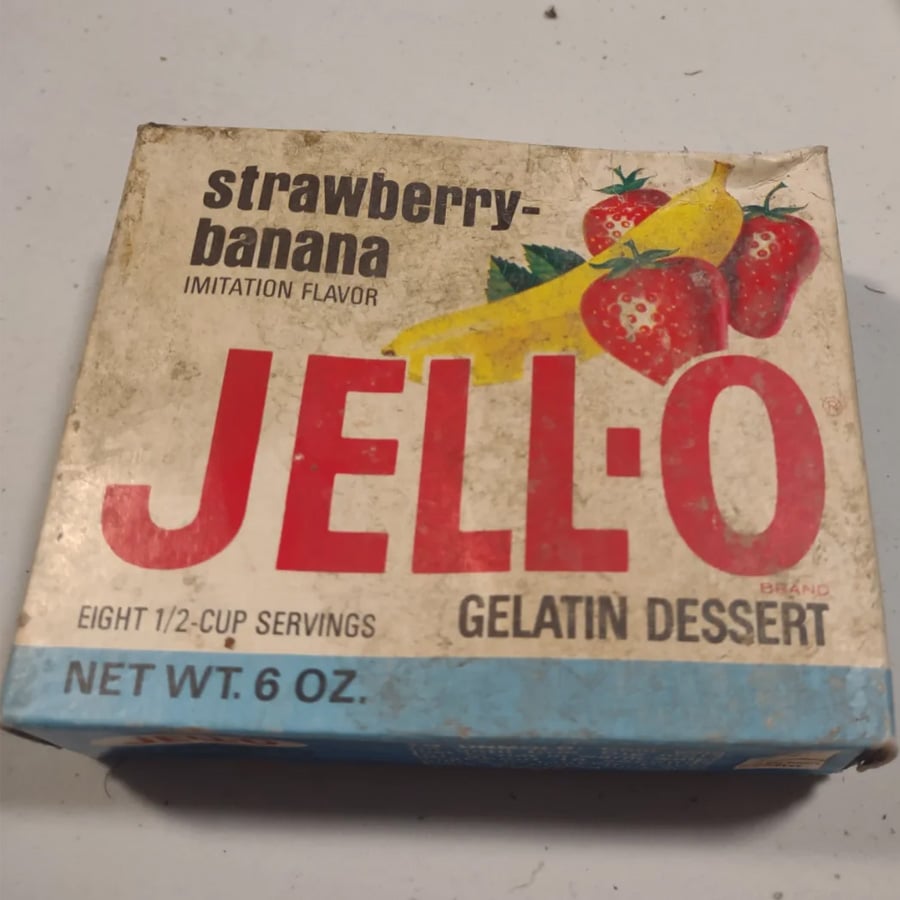 Vintage box of strawberry-banana flavor Jell-O gelatin dessert, 6 oz, with images of strawberries and bananas on the package. The box shows slight wear and faded colors, indicating it is old.