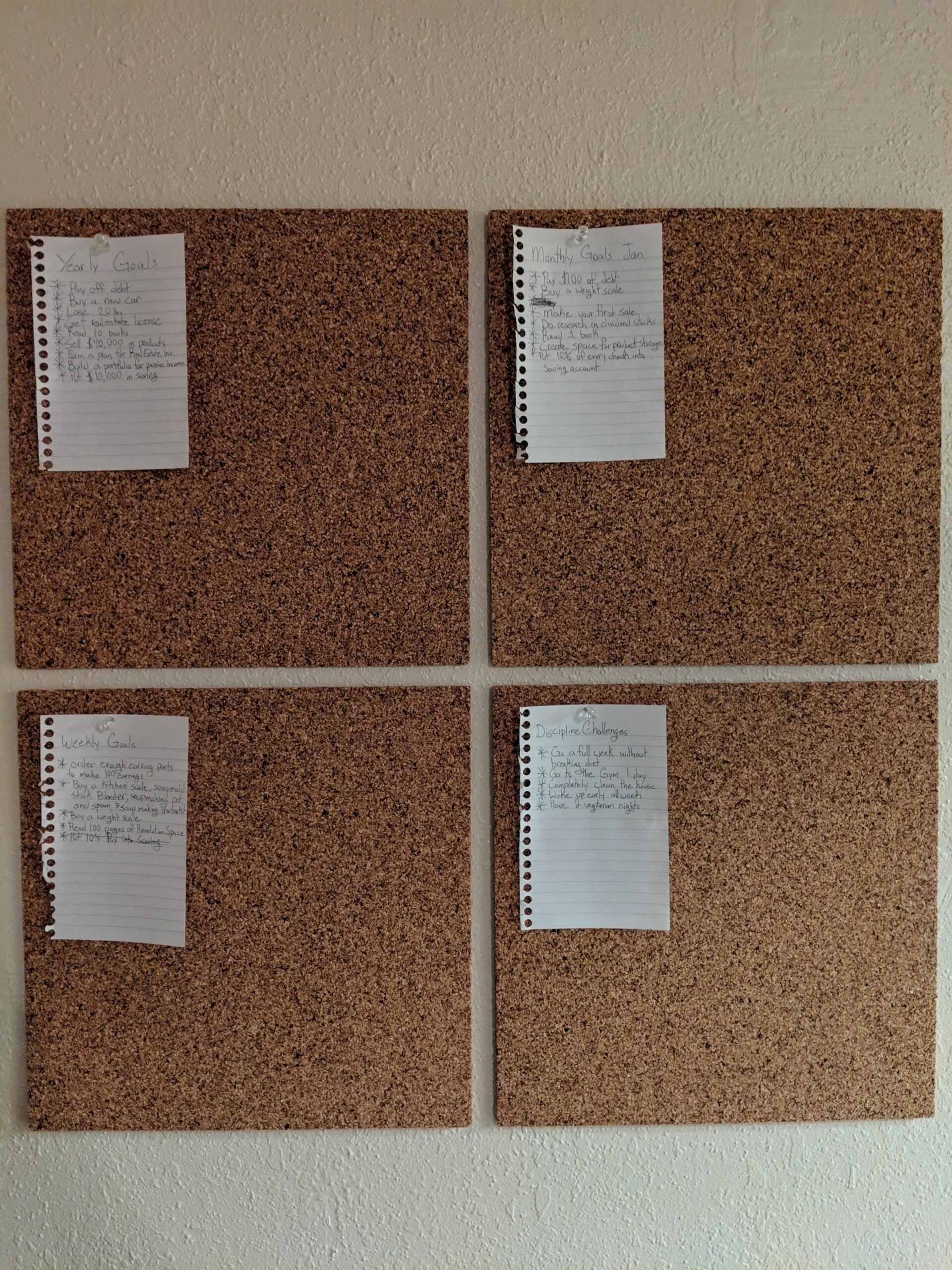 Four cork boards arranged in a square on a wall. Each board has a handwritten page pinned at the top left, with lists titled “Yearly Goals,” “Monthly Goals,” “Weekly Goals,” and “Daily Challenges.”