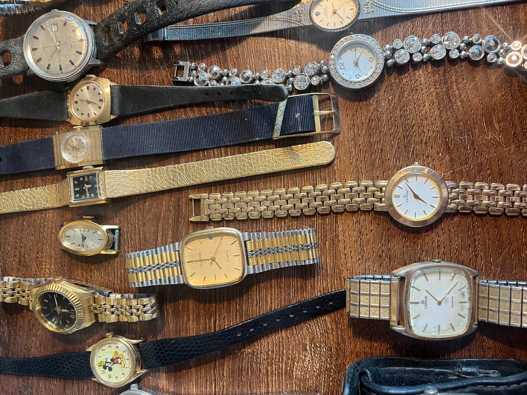 A collection of vintage wristwatches with metal and leather bands is displayed on a wooden surface, featuring various sizes, shapes, and colors.