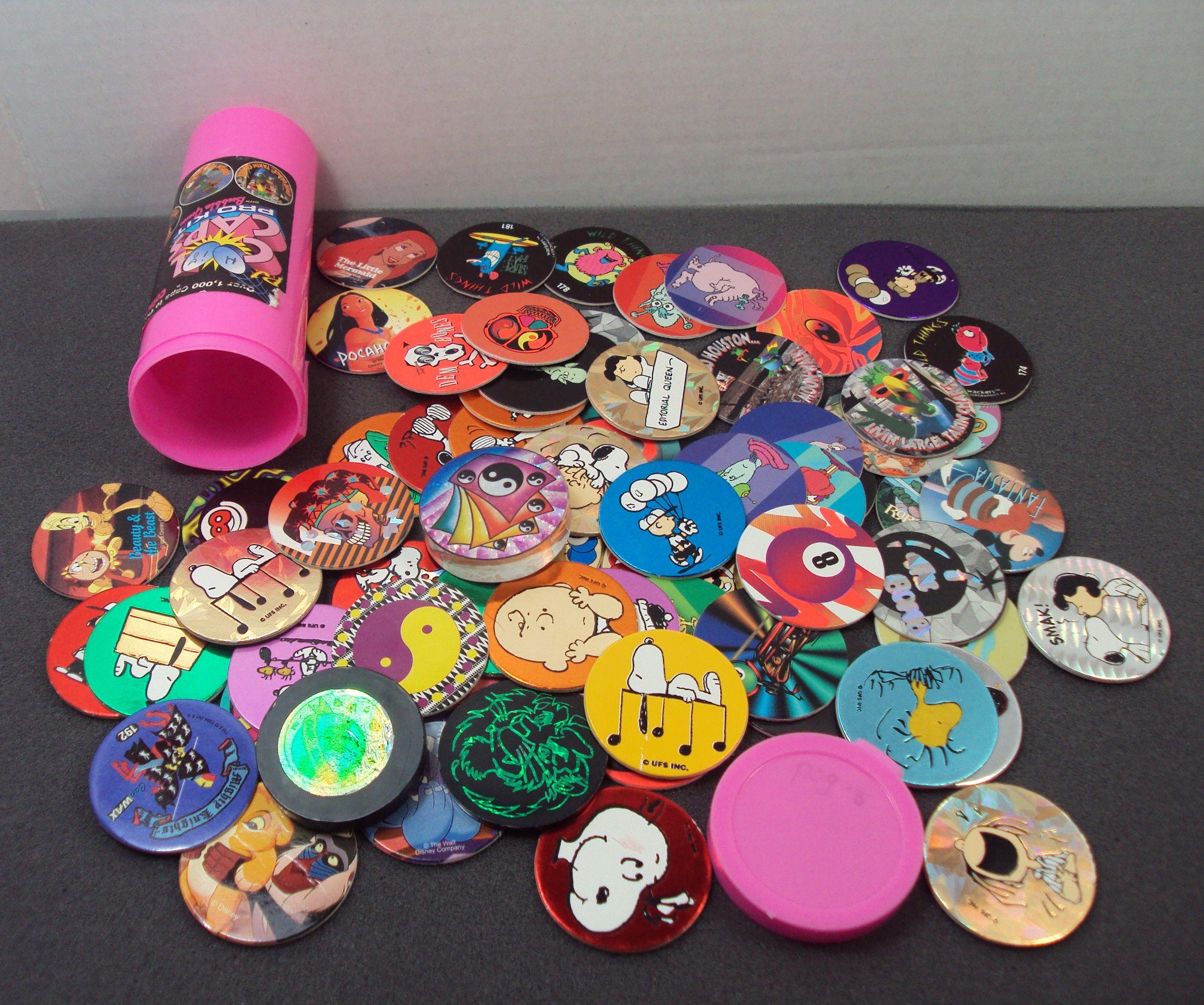 A pile of colorful Pogs with various cartoon designs is spread out on a surface next to a pink container.