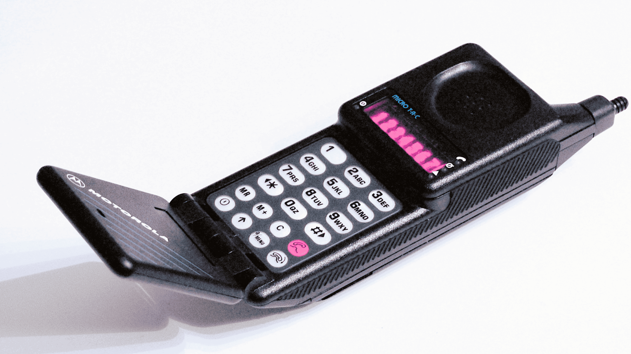 A black Motorola flip phone with a physical keypad and small screen is open, showing buttons with numbers and symbols. The phone is angled on a white background.
