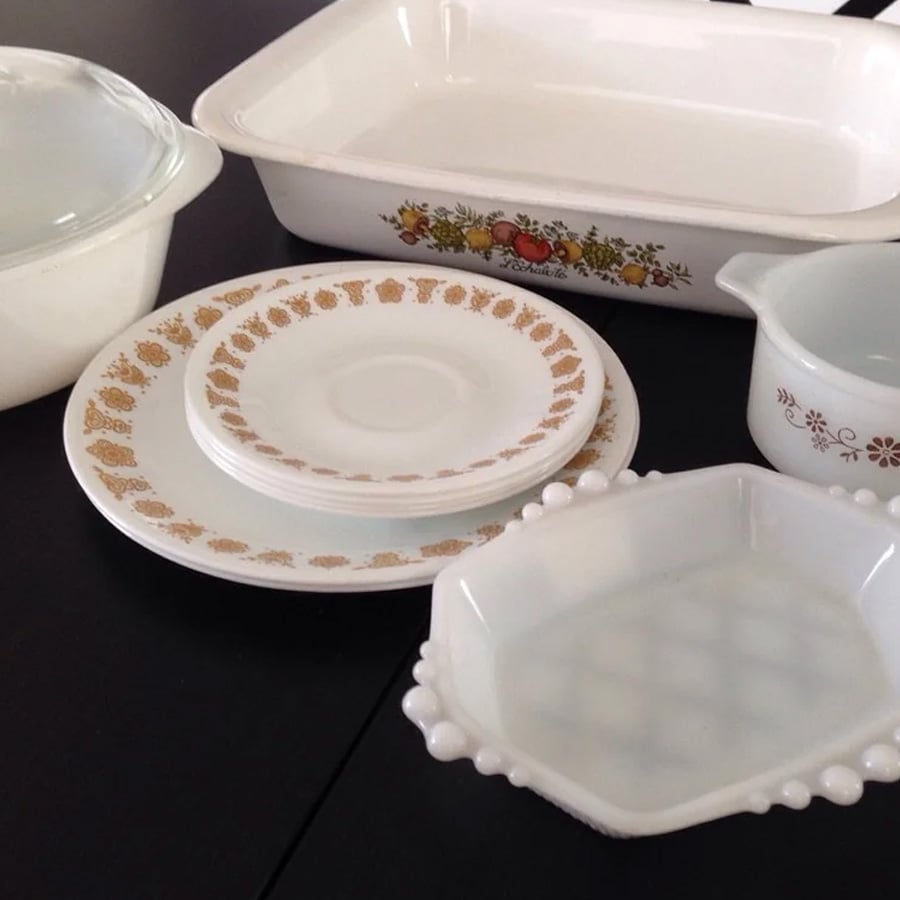 A collection of vintage white dishes and bakeware with assorted patterns, including floral and gold designs, displayed on a dark surface.
