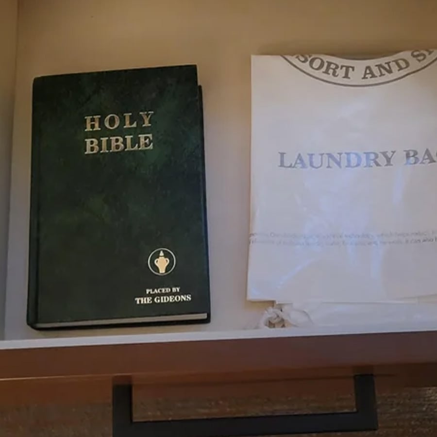 A Holy Bible placed by The Gideons is on the left side of a drawer, next to a white laundry bag on the right.