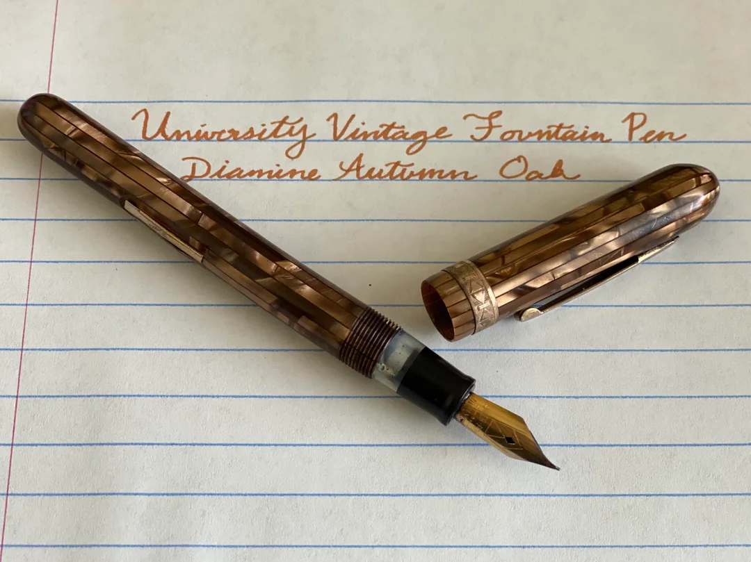 A brown marbled fountain pen with the cap off rests on lined paper. Copper-colored writing above reads, “University Vintage Fountain Pen Diamine Autumn Oak.”