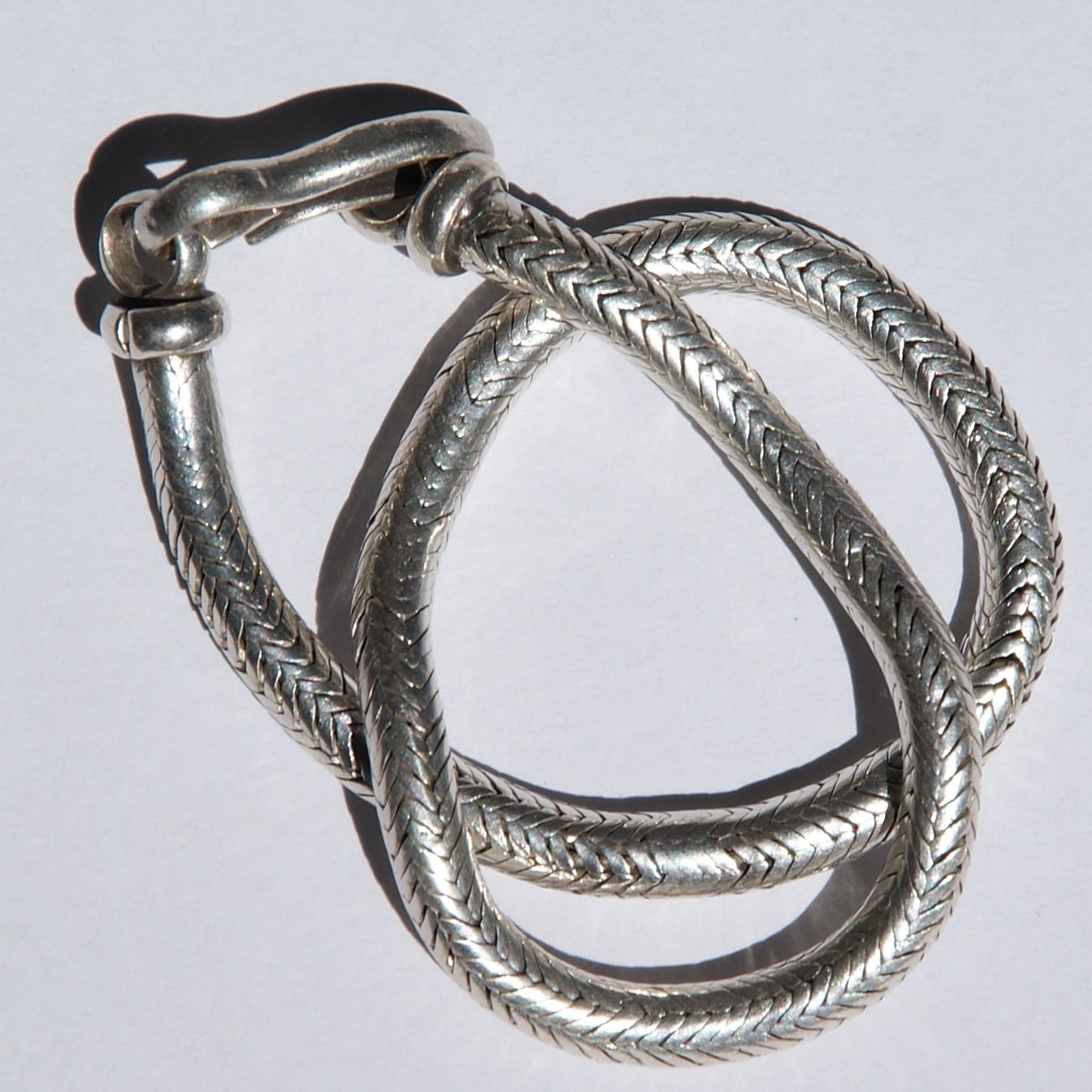 A silver, textured bracelet with a woven pattern, curled into overlapping loops on a white background.