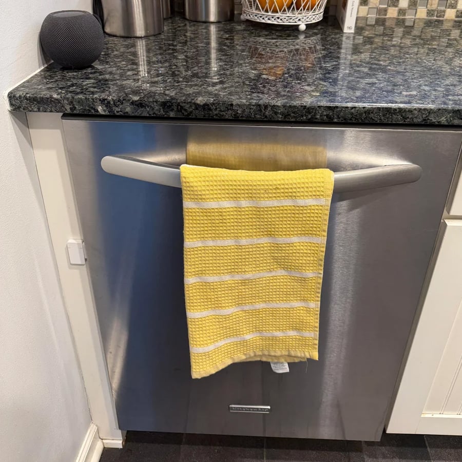A yellow and white striped towel hangs on the handle of a stainless steel dishwasher beneath a granite countertop in a modern kitchen.