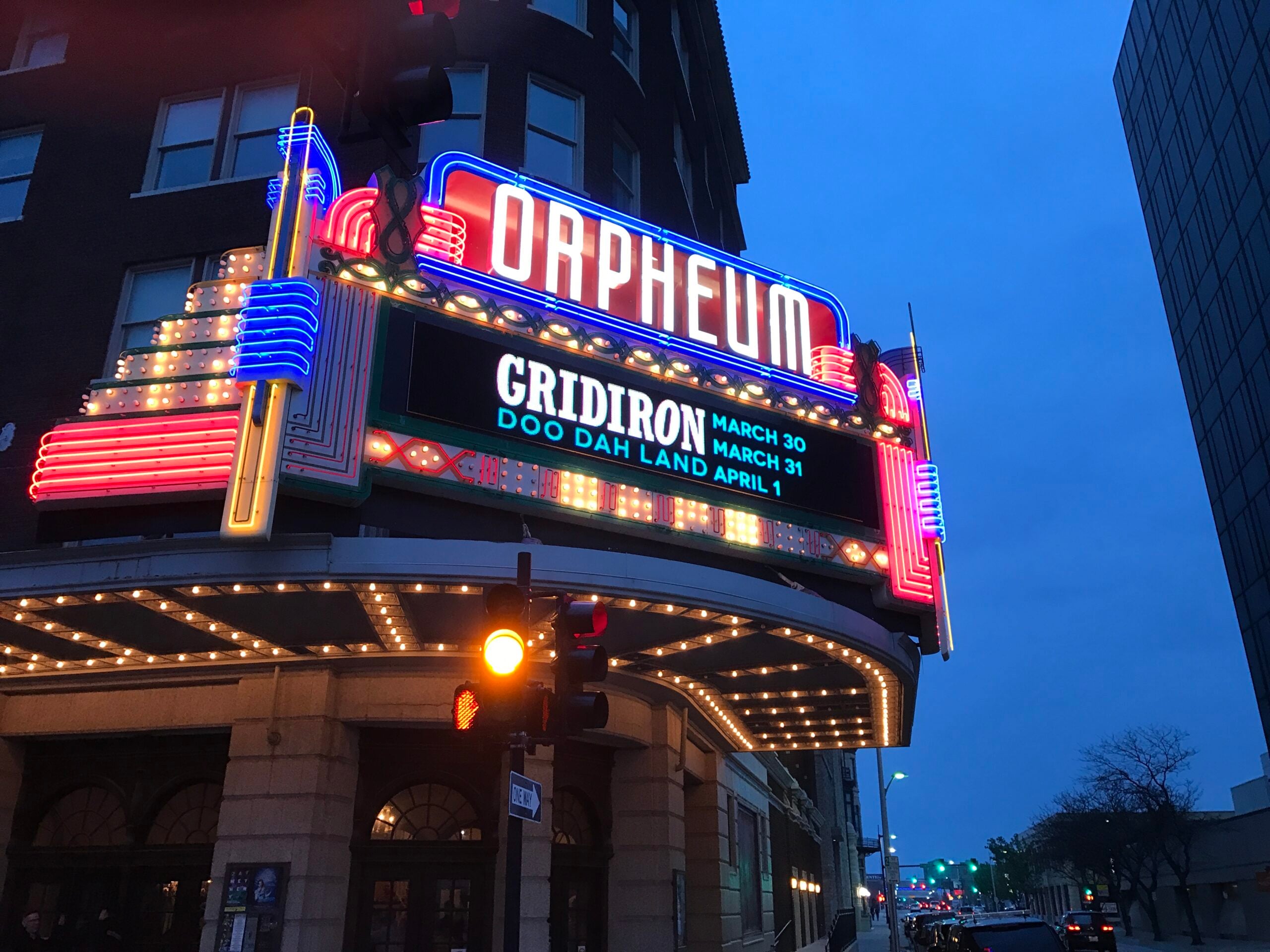 The Orpheum Theater’s lit marquee advertises events: “GRIDIRON March 30, March 31” and “DOO DAH LAND April 1.” The building and street are visible at dusk under a blue sky.