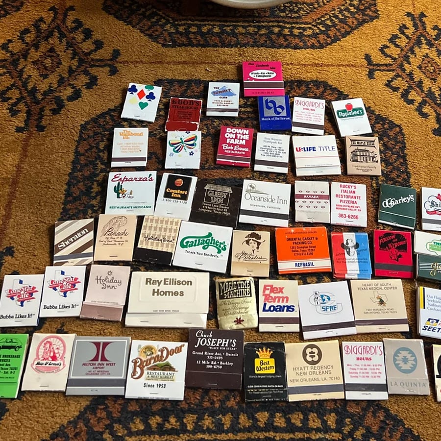 A collection of colorful vintage matchbooks from various restaurants and hotels is arranged in a grid pattern on a patterned carpet.