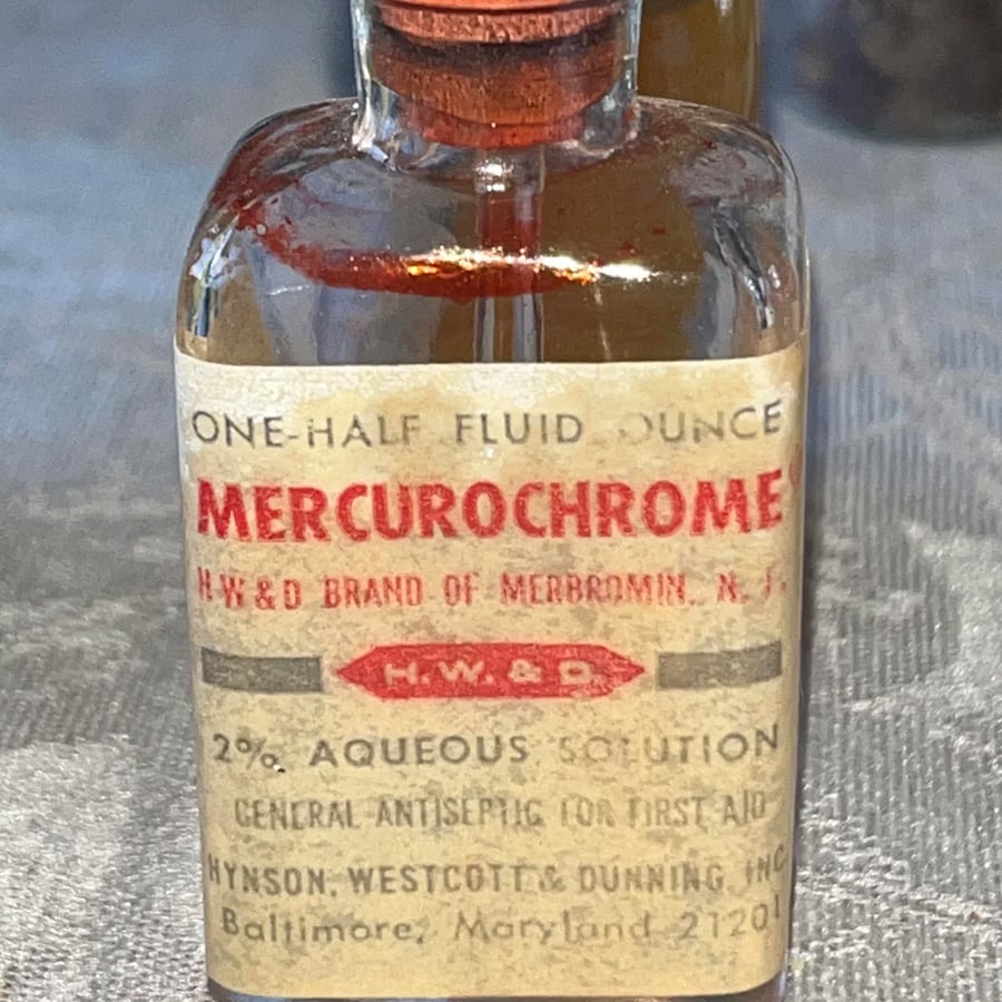 A small vintage bottle labeled “Mercurochrome” with a red cap, containing a 2% aqueous solution for first aid, produced by Hynson, Westcott & Dunning, Inc., Baltimore, Maryland.