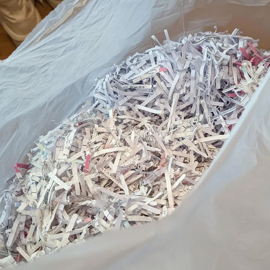 A plastic bag filled with shredded paper strips, some with visible text and hints of color, viewed from above.