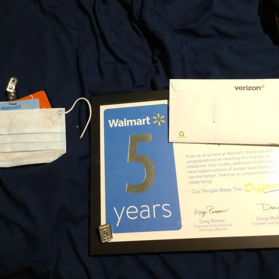 A Walmart 5 years plaque, a congratulatory letter, a Verizon envelope, a metal pin, a clip, and a face mask are placed on a dark blue surface.