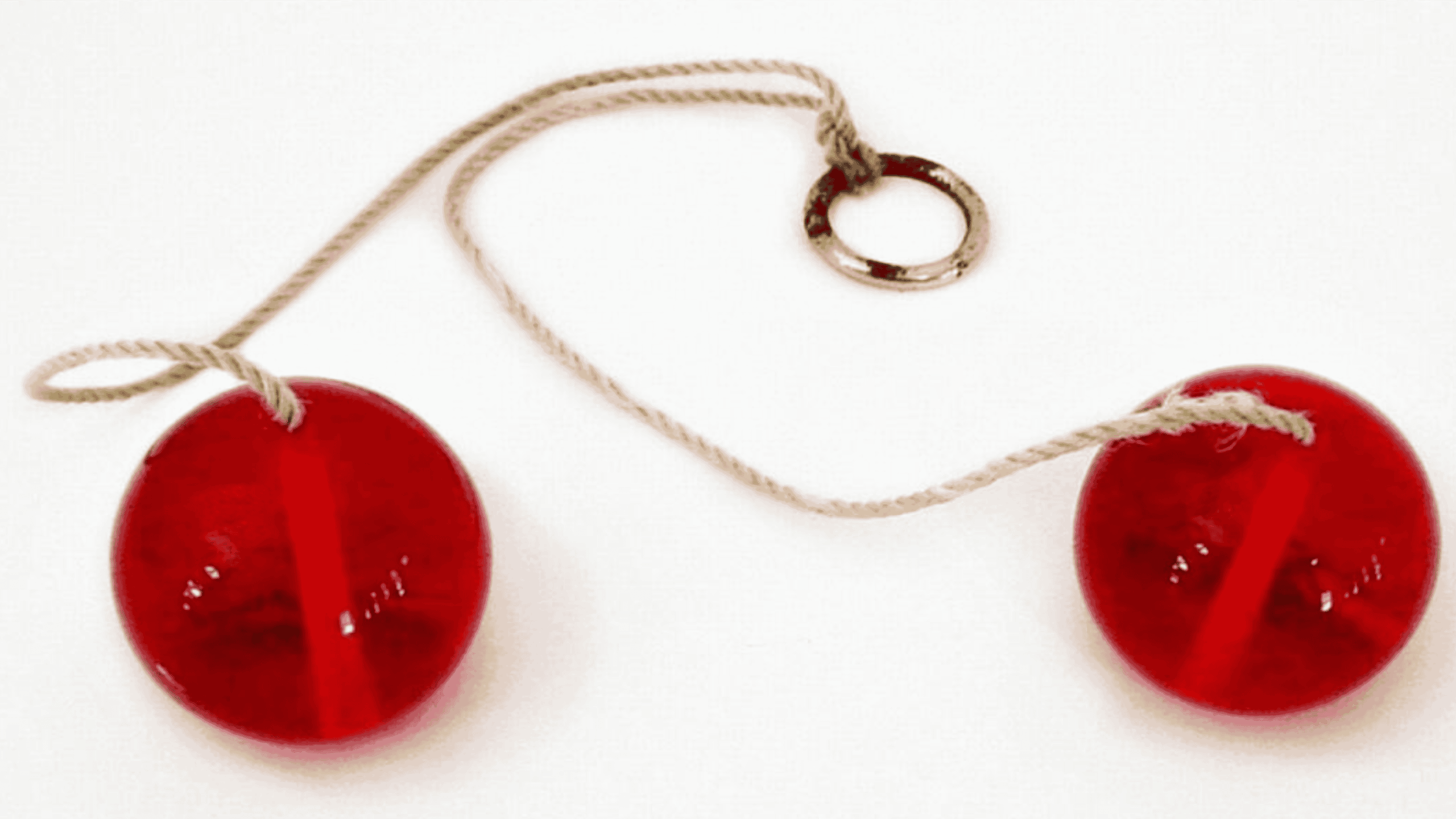 Two red plastic balls connected by a string with a metal ring attached in the middle, laid out on a white surface.
