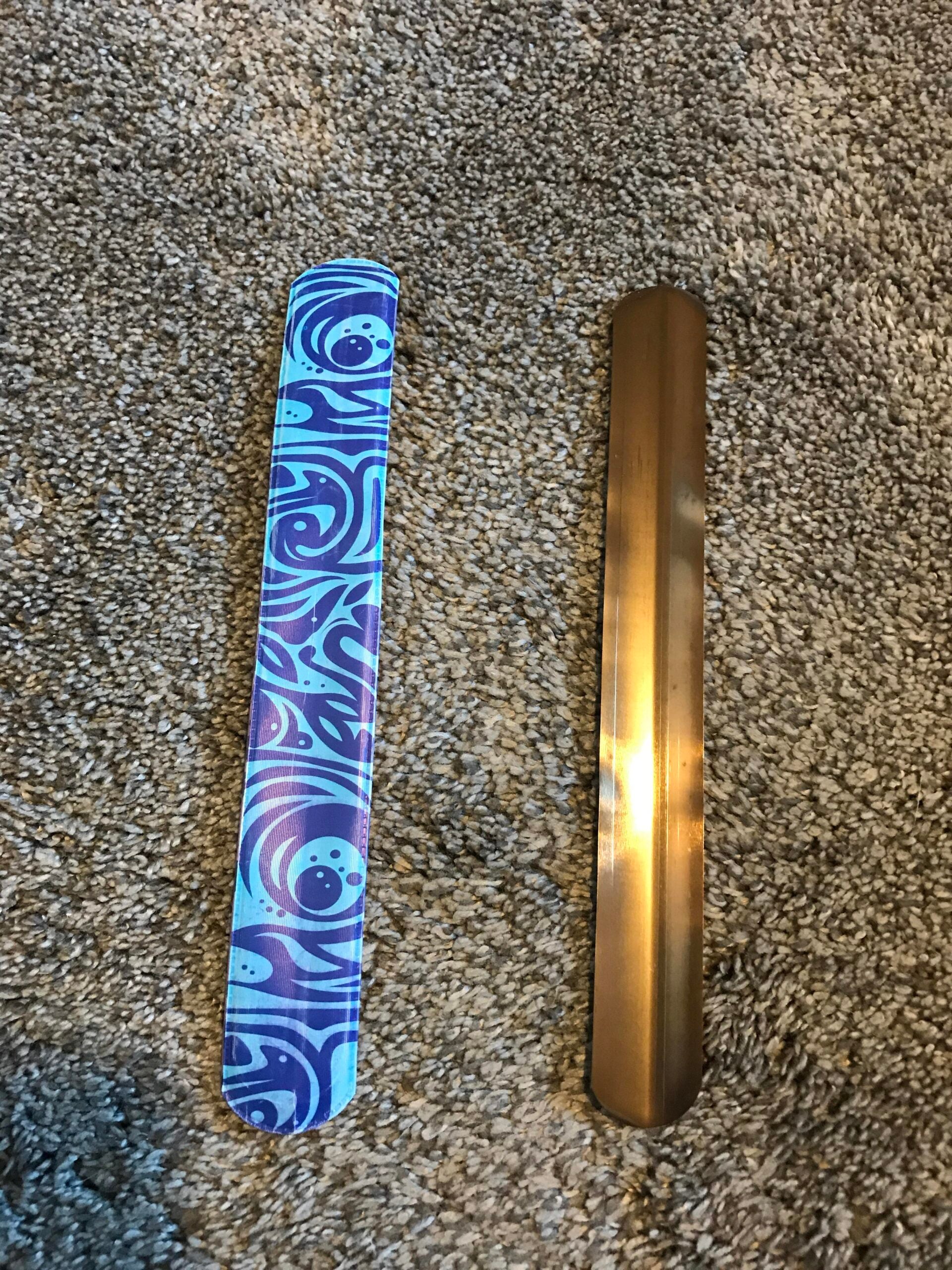 Two slap bracelets lie on a carpet: one has a blue and purple swirl pattern, and the other is plain metallic gold.