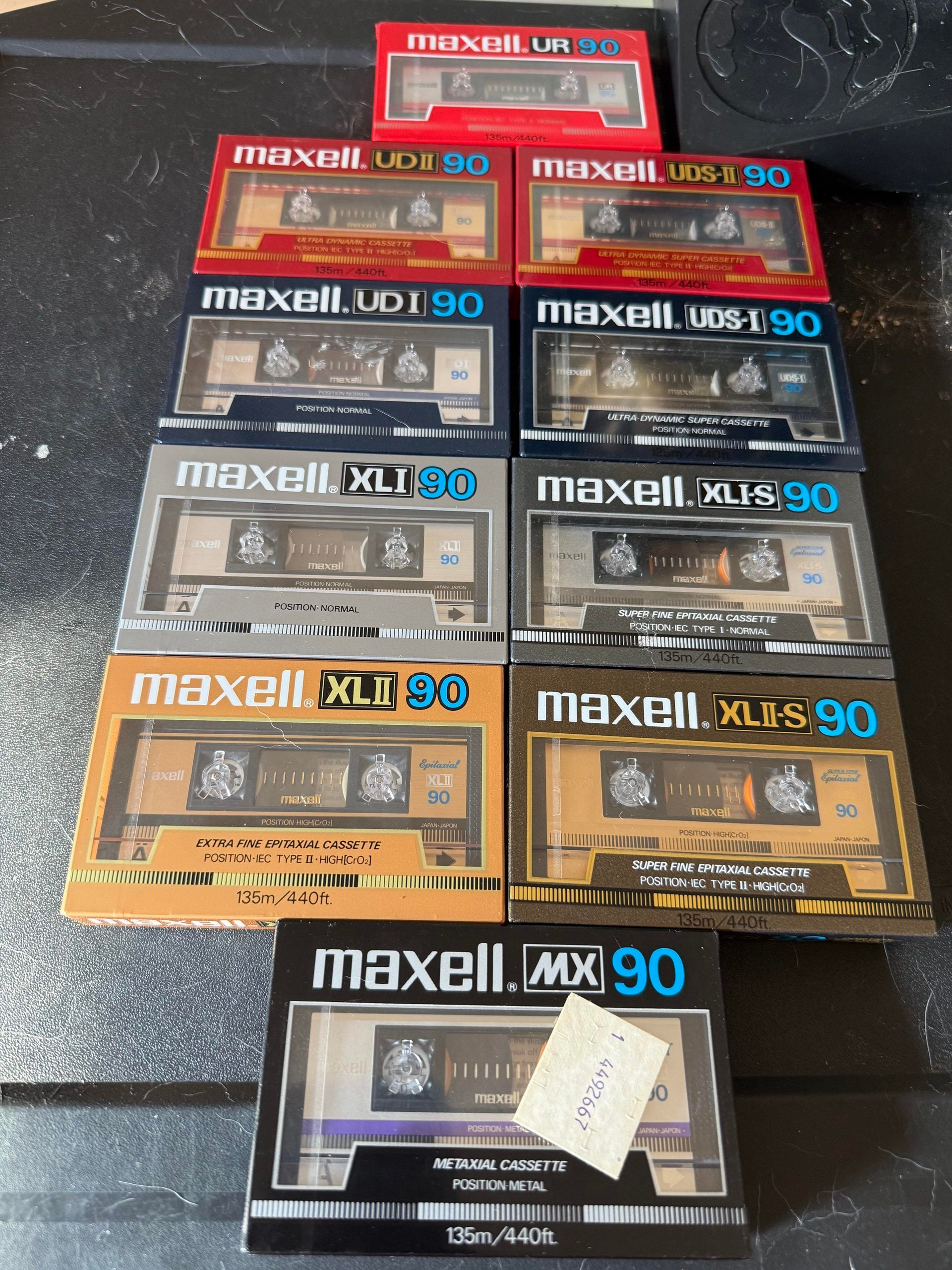 Ten Maxell audio cassette tapes in various colored cases are arranged neatly on a black surface, with labels showing different models including UR, UDI, XLII, XLS, and MX.