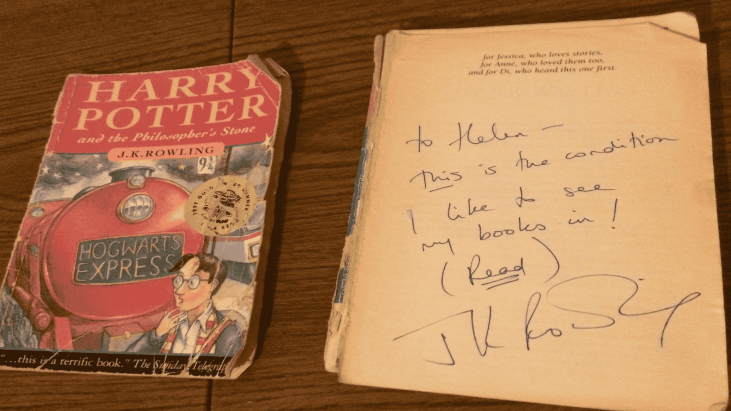 A worn copy of “Harry Potter and the Philosopher’s Stone” lies next to an open page inscribed with a handwritten message and signature from J.K. Rowling. The books rest on a wooden surface.